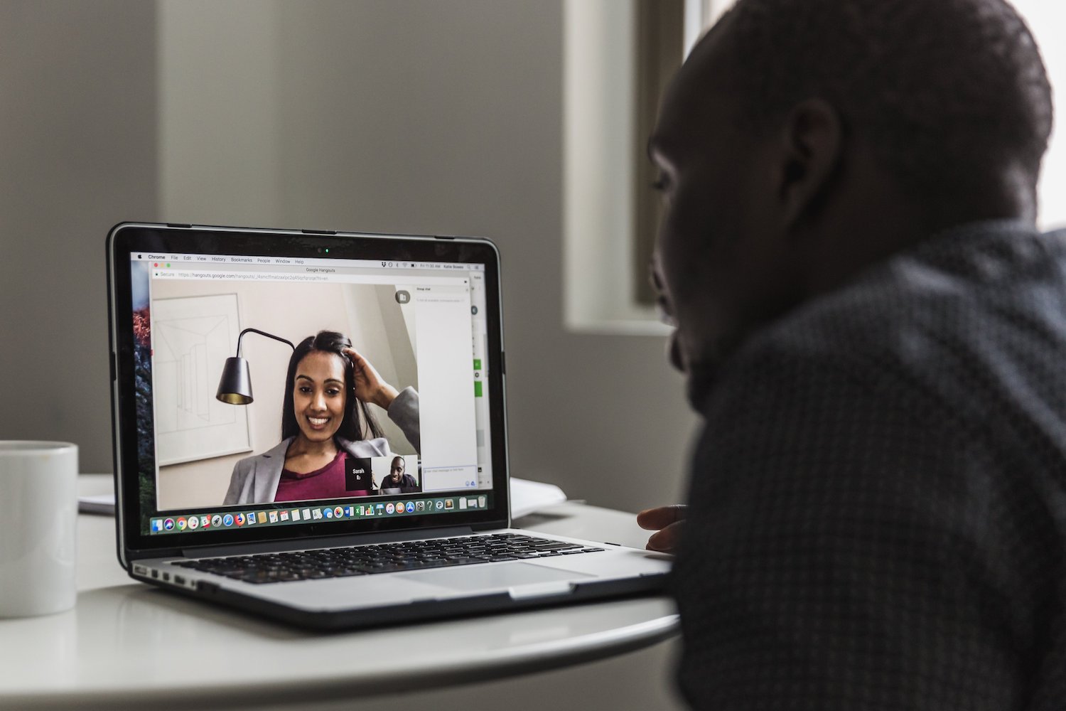 This is an image of a video conference call chat. A woman in a blazer is seen smiling on the screen while a man is talking into his computer microphone. This is a visualization of the human element in customer support.