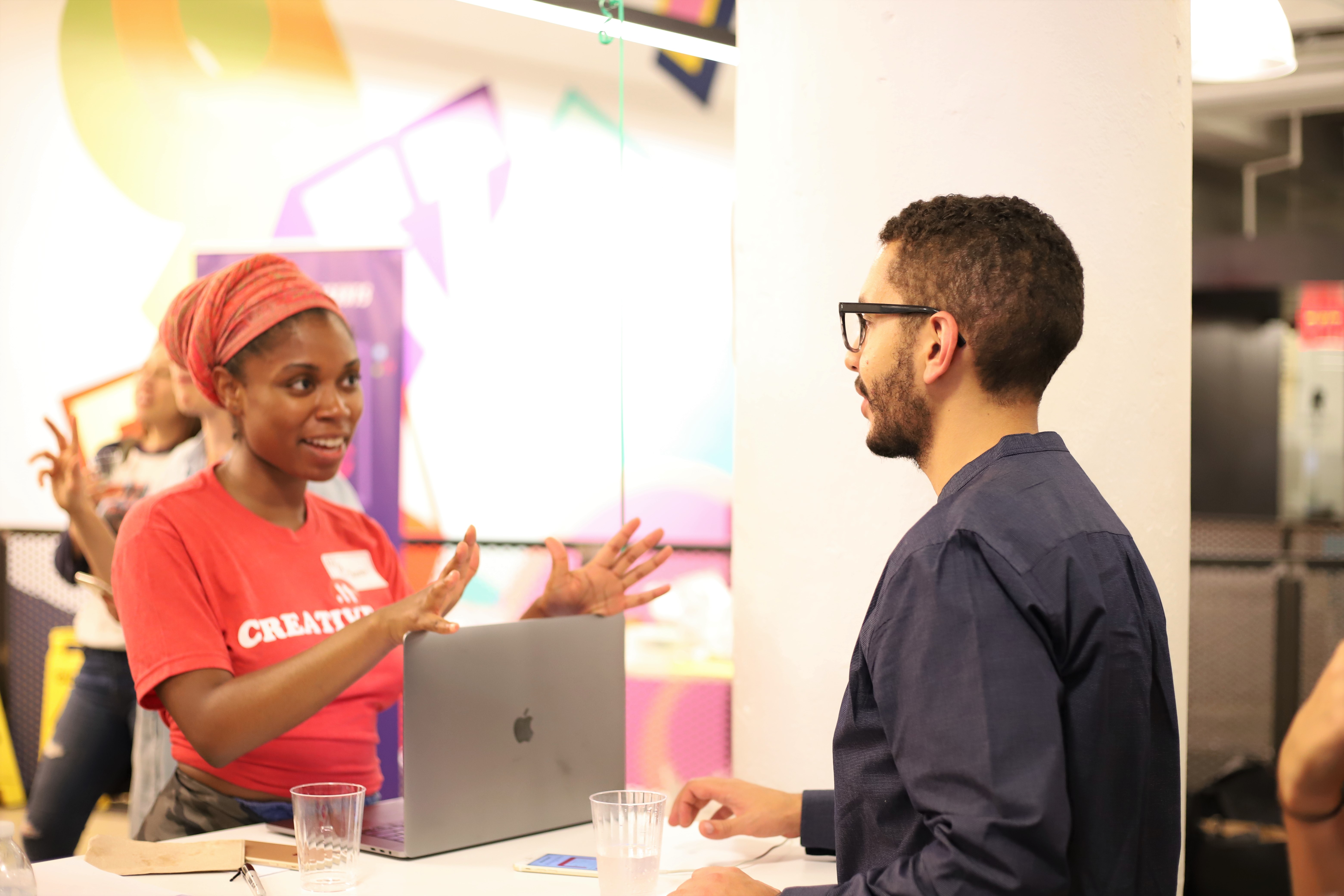 This is an event photo of a user testing event. This image shows a woman talking to a man about UX. This image features women and people of color in tech at a user testing event.
