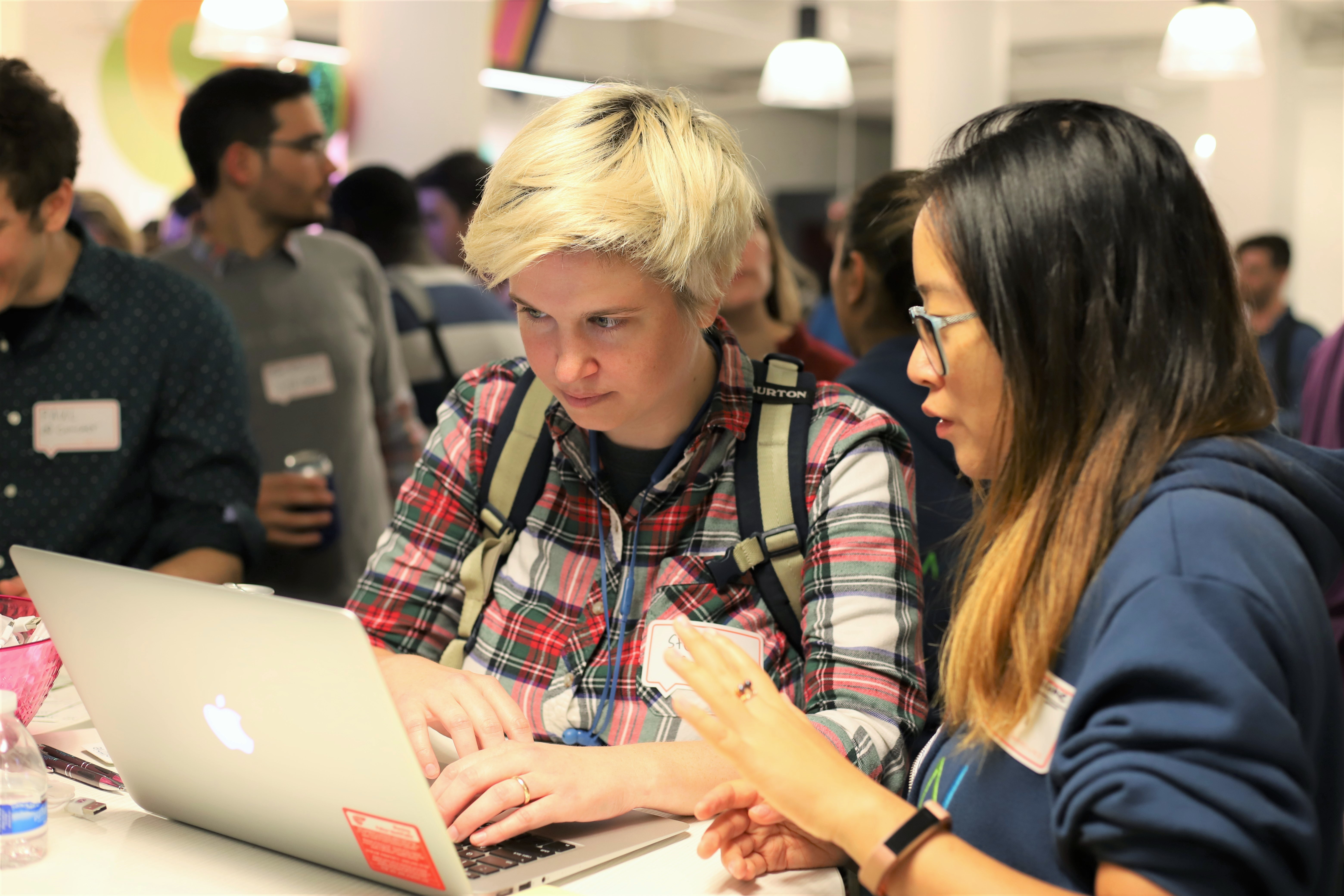 This photo shows a woman with short blonde hair testing softwareat a user testing event while she talks to a woman with dark hair who is explaining the product.
